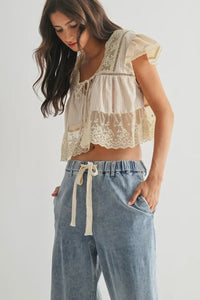 Woman wearing a lace top and light blue pants on a plain background