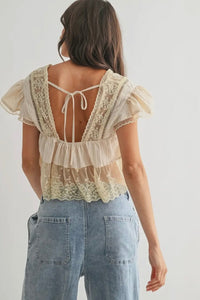 Woman wearing a lace top with ruffled sleeves and open back, standing against a plain background.