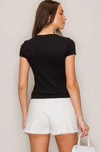 Load image into Gallery viewer, A woman shown from the back wearing a fitted black short-sleeve top and white shorts, holding a white handbag against a plain light background.