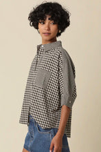Load image into Gallery viewer, A model with short curly black hair wearing a black and white gingham checkered shirt with rolled-up sleeves and blue denim shorts, posed against a solid beige background.