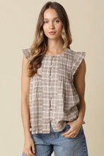 Load image into Gallery viewer, A woman wearing a sleeveless button-front top with a beige and brown plaid pattern and ruffled shoulder details, paired with blue jeans, against a solid beige background.