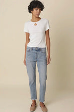 Load image into Gallery viewer, A model wearing a white short-sleeve ribbed knit top with a circular cutout at the collar, paired with light-wash blue jeans and beige flats, standing against a solid beige background.
