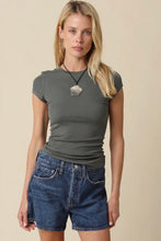 Load image into Gallery viewer, A blonde woman modeling a fitted short-sleeve crewneck t-shirt in dark olive green, paired with blue denim shorts, against a solid beige background.