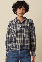 Load image into Gallery viewer, A model wearing a navy blue and beige plaid button-up shirt with blue jeans, standing against a solid beige background.
