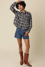 Load image into Gallery viewer, A model wearing a dark blue and white plaid button-down shirt, denim shorts, and brown leather cowboy boots, posing against a solid beige studio background.