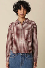 Load image into Gallery viewer, A model with short curly black hair wearing a long-sleeve button-up shirt in a brown and white gingham pattern, paired with blue jeans, against a solid beige background.