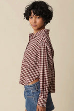 Load image into Gallery viewer, A model wearing a cropped, long-sleeve button-up shirt with a brown and white gingham check pattern, paired with blue denim shorts, set against a plain beige background.