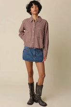 Load image into Gallery viewer, A model stands against a plain beige studio background wearing a cropped, long-sleeve button-up shirt in a brown and white gingham pattern, a blue denim mini skirt, and dark brown leather boots.