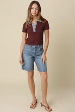 Load image into Gallery viewer, A woman modeling a short-sleeve polo shirt in dark burgundy with a light blue collar detail, paired with light-wash denim shorts and brown heeled sandals, against a solid beige studio background.