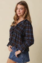 Load image into Gallery viewer, A woman modeling a dark brown and blue plaid long-sleeve blouse with a smocked bodice and tie neckline, paired with a denim mini skirt, against a solid beige background.