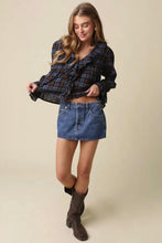 Load image into Gallery viewer, A woman modeling a dark blue and brown plaid long-sleeve blouse with a ruffled collar, paired with a blue denim mini skirt and dark brown knee-high boots, against a solid beige background.