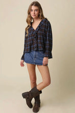 Load image into Gallery viewer, A woman modeling a dark blue and black plaid long-sleeve blouse with a ruffled front, paired with a denim mini skirt and dark brown ankle boots, against a solid beige background.