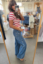 Load image into Gallery viewer, A woman takes a mirror selfie in a clothing boutique, wearing a red and white striped short-sleeve t-shirt and high-waisted, wide-leg blue denim jeans.