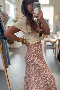 Person taking a mirror selfie wearing a white top and floral skirt in a store.