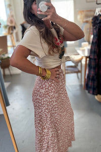 Person taking a mirror selfie wearing a beige top and floral skirt in a store.