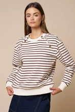 Load image into Gallery viewer, A woman modeling a long-sleeve crewneck sweater with thin brown and cream horizontal stripes, featuring decorative brown buttons on the shoulders and cuffs, paired with dark blue jeans against a solid beige background.