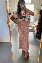 Load image into Gallery viewer, Person taking a mirror selfie wearing a graphic t-shirt and floral skirt in a room with a mirror and clothing rack.