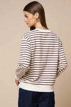 Load image into Gallery viewer, A woman shown from the back wearing a cream-colored long-sleeve sweatshirt with thin dark brown horizontal stripes and dark navy blue pants, set against a solid beige studio background.