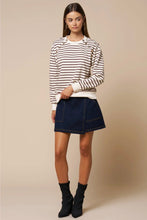 Load image into Gallery viewer, A woman modeling a cream and dark brown horizontally striped long-sleeve crewneck sweater, paired with a dark blue denim mini skirt and black ankle boots, against a solid beige studio background.