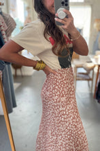Load image into Gallery viewer, Person taking a mirror selfie wearing a white t-shirt with a graphic design and a floral skirt in a clothing store.
