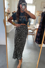 Load image into Gallery viewer, Person taking a mirror selfie wearing a dark floral skirt and crop top in a room with clothing racks.