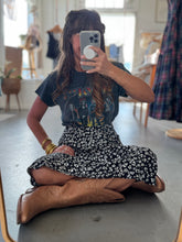 Load image into Gallery viewer, Person sitting on the floor taking a mirror selfie wearing a graphic t-shirt, floral skirt, and brown boots.