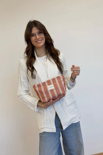 Woman holding a striped clutch against a plain background