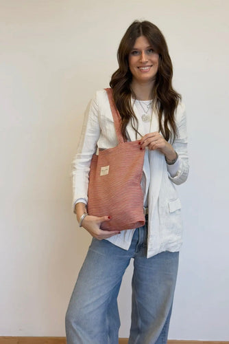Woman holding a pink striped tote bag against a white background