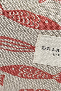 Fabric with red fish pattern and 'DE LA' label on a beige background