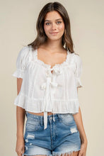 Load image into Gallery viewer, A woman wearing a white short-sleeve lace-up blouse with ruffles and blue distressed denim shorts, standing against a plain beige studio background.