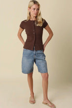 Load image into Gallery viewer, A woman modeling a dark brown short-sleeve button-front top and light-wash denim shorts against a plain beige studio background.
