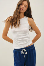 Load image into Gallery viewer, A woman wearing a fitted white sleeveless crop top and blue drawstring sweatpants, photographed against a plain light gray studio background.