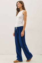 Load image into Gallery viewer, A woman modeling wide-leg navy blue lounge pants with a white tank top and brown slip-on shoes, standing against a plain off-white studio background.