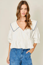 Load image into Gallery viewer, Woman wearing a white blouse with blue trim and blue jeans on a beige background