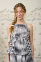 Load image into Gallery viewer, Woman wearing a black and white checkered dress against a floral wallpapered wall.