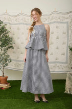 Load image into Gallery viewer, Woman wearing a black and white checkered dress standing in front of a decorative wall with plants.