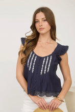Load image into Gallery viewer, Woman wearing a navy blue top with white embroidery and ruffles, holding a straw hat.