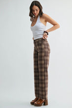 Load image into Gallery viewer, A woman modeling a pair of brown and beige plaid wide-leg pants with a white halter top and brown platform heels, standing against a light gray studio background.