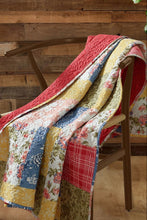 Load image into Gallery viewer, A multicolor patchwork quilted throw blanket draped over a wooden chair in front of a rustic wood-paneled wall.
