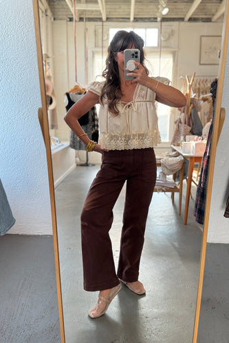 Person taking a mirror selfie wearing a beige lace top and brown pants in a room.