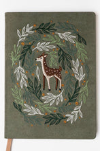 Load image into Gallery viewer, A hardcover notebook with a dark olive green cover featuring an embroidered design of a brown deer surrounded by a wreath of green and white leaves with small orange berries. A light tan ribbon bookmark is visible at the bottom left, set against a plain white background.