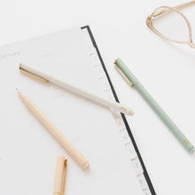 Load image into Gallery viewer, Two minimalist ballpoint pens, one in warm cream and one in sage green, with gold accents, arranged on a white planner page alongside a pair of eyeglasses.