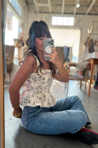Person taking a mirror selfie wearing a patterned top and blue jeans in an indoor setting.