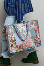 Load image into Gallery viewer, A person wearing a blue and white striped shirt, ripped light-wash jeans, and dark green boots carries a large patchwork tote bag with floral and striped fabric panels.