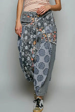 Load image into Gallery viewer, A person wearing loose, patchwork-patterned harem-style pants with gray floral and striped panels, paired with a light pink top and black-and-white sneakers, against a plain light gray studio background.