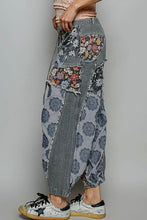 Load image into Gallery viewer, A person wearing loose, patchwork-style harem pants with gray striped and floral fabric panels, paired with white sneakers, photographed against a plain light gray studio background.