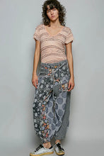 Load image into Gallery viewer, A model stands against a light gray studio background wearing a light pink textured short-sleeve top, gray patterned harem-style pants with floral and paisley prints, and white sneakers with black laces.