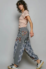 Load image into Gallery viewer, A model wearing a light pink ruffled short-sleeve top and gray patchwork cargo pants with floral details, paired with white sneakers, against a solid gray studio background.