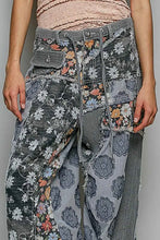 Load image into Gallery viewer, A close-up of a person wearing patchwork wide-leg jeans with mixed floral, striped, and textured fabric panels in gray, white, and muted floral tones, paired with a light pink ribbed top.