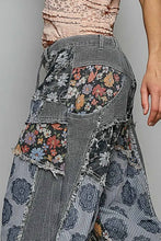 Load image into Gallery viewer, A close-up of a person wearing a pair of patchwork wide-leg jeans with mixed patterns including floral prints, vertical stripes, and frayed denim details. The model is also wearing a light pink lace top, shown against a plain gray background.